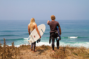 Two surfers with boards about to hit the waves at Ericeira, Europe's World Surfing Reserve.