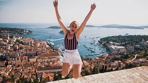 Person mid jump with their hands in the air with the city of Hvar behind them.