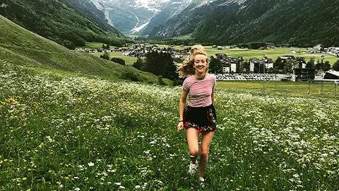 Person running in the grass of a European village nestled in between mountains.