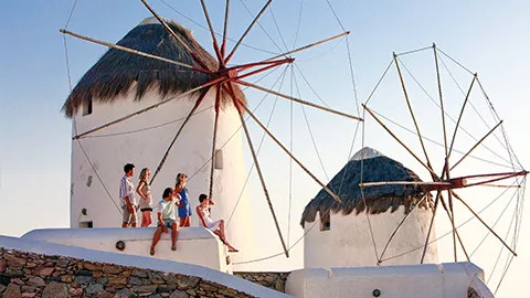 People standing together with two of the windmills of Mykonos behind them.