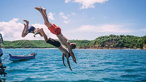 Three people diving from a boat into the ocean with their arms stretched out.
