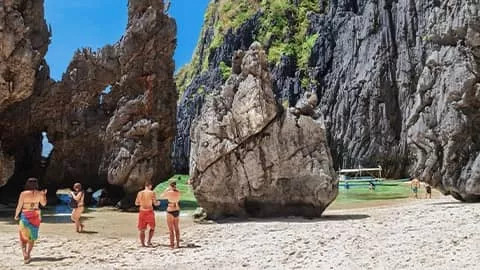 People standing on the beach near large limestone rock formations.