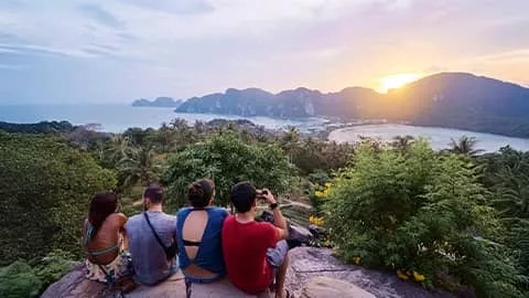 People sitting on a rock lookout while the sun comes up over the Phi Phi islands in Thailand.
