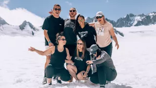 Seven people smiling while standing on a white glacier in the South Island of New Zealand.