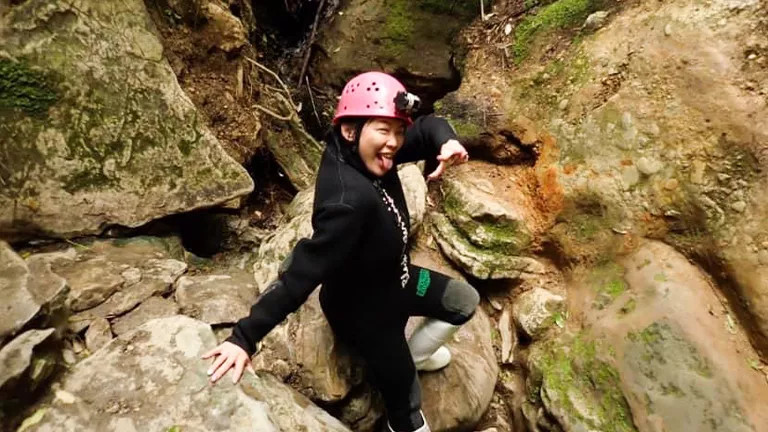 Person wearing a wetsuit and a helmet poses while caving in New Zealand.
