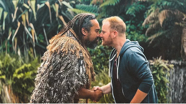 Two people greeting each other with traditional Maori hongi by touching their noses while shaking hands.