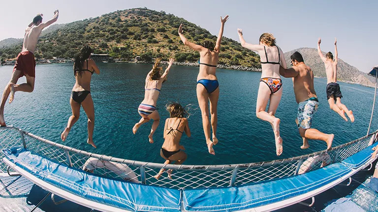 Eight people jump from a sail boat railing into the ocean.