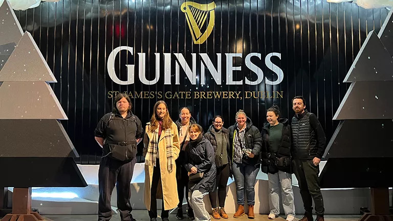 Group of people posing together in front of the St James Gate Guinness sign at Christmas time.