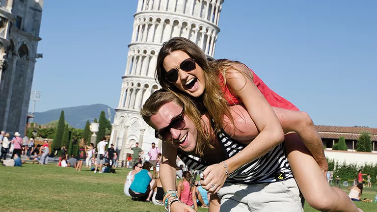 Person giving another a piggy back ride in front of the Leaning Tower of Pisa.