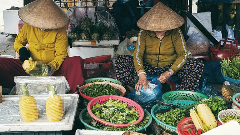 Two people prepare fresh produce for sale at a local market in Hoi An, Vietnam.