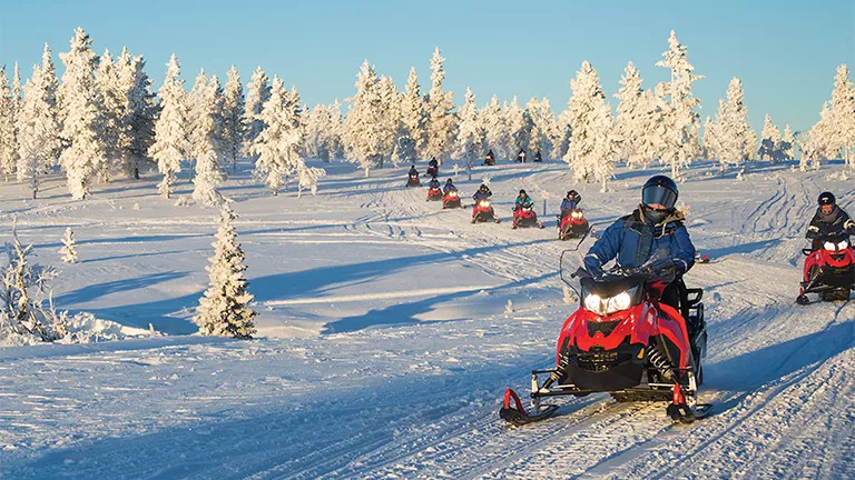 People riding snowmobiles in a single file line across a snow covered landscape.