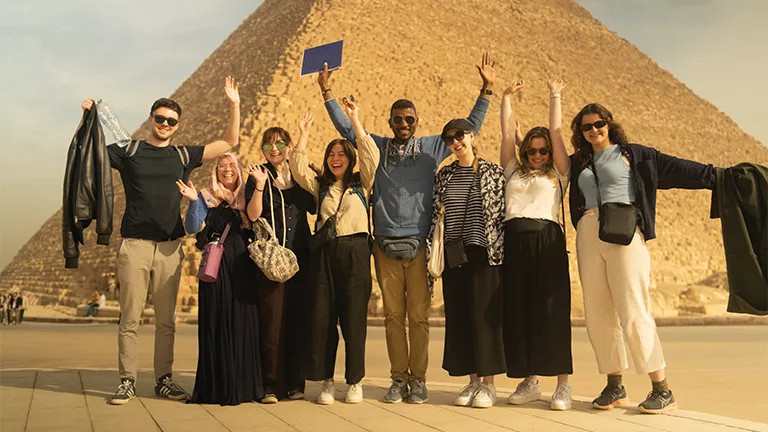 A group of people standing together with their hands in the air in front of the pyramids in Eygpt.