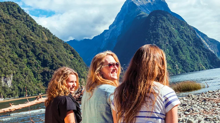 Three people standing on the stoney shore of Milford Sound.