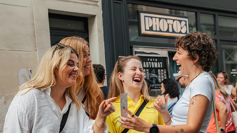 People laugh together while looking at photos taken in a photobooth in Paris.
