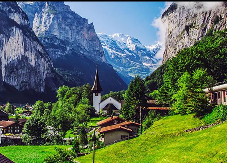 A wide view of a small hamlet in Switzerland in the valley of it's vast mountainscape.