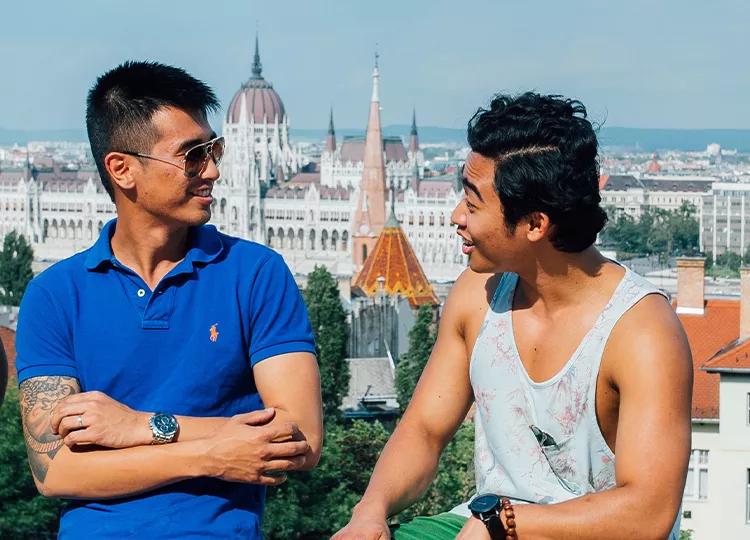 A group of Topdeck travelers chatting with each other in Budapest, with the Hungarian Parliament in the background.