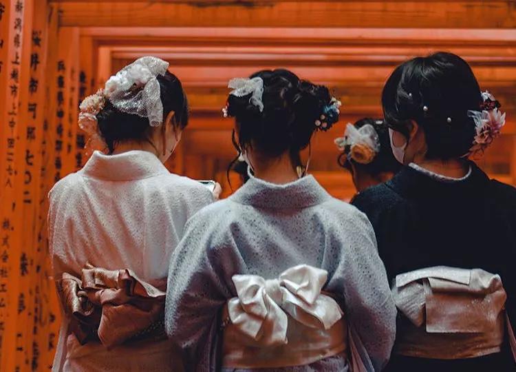 Three ladies in a kimono walking under Torii gates at the Fushimi Inari Shrine.