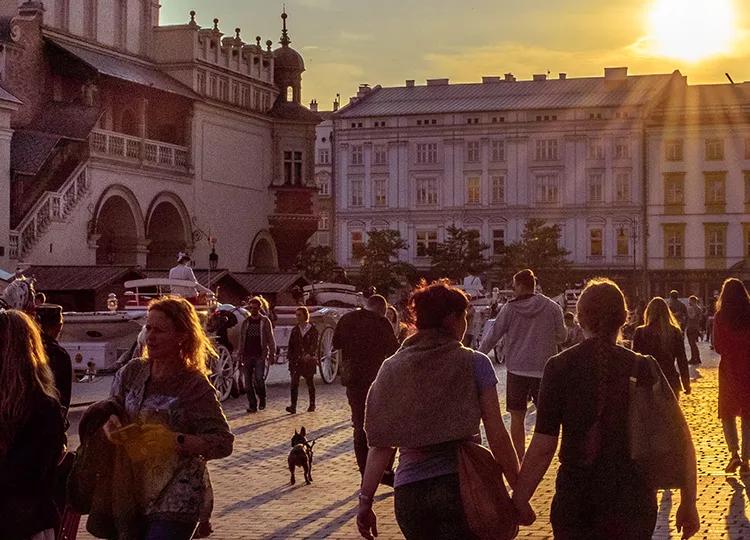 People and horse drawn carriages enjoy Krakow's old city streets as the sun sets.