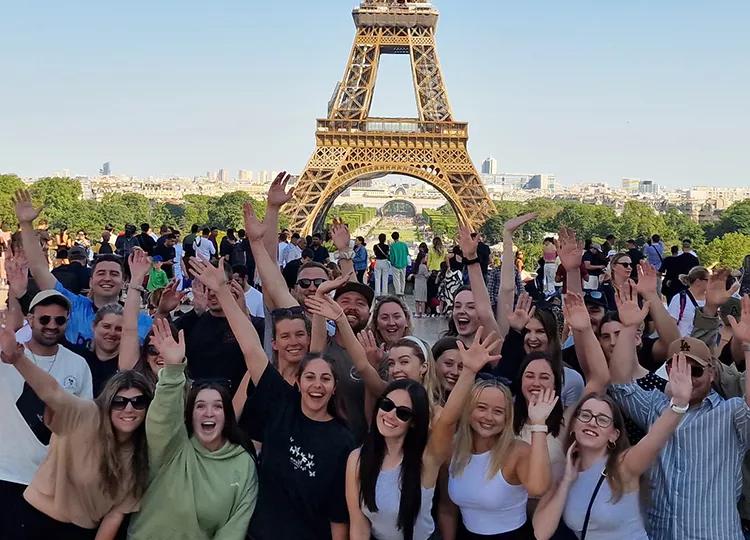 Topdeck tour group smiling and posing for a group photo in front of the famous Eiffel Tower of Paris.