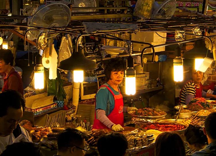 People selling and purchasing various foods and ingredients at Gwanjang Market, the oldest and one of the largest traditional markets in South Korea.