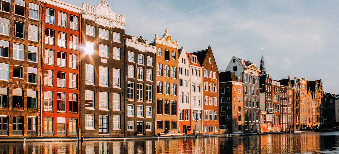 Street of large colourful houses on a canal in Amsterdam. The sun reflects off a window.