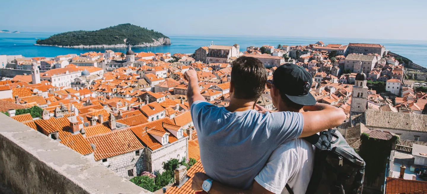 Two people with their arms around each other look out over orange rooves of Croatian town.