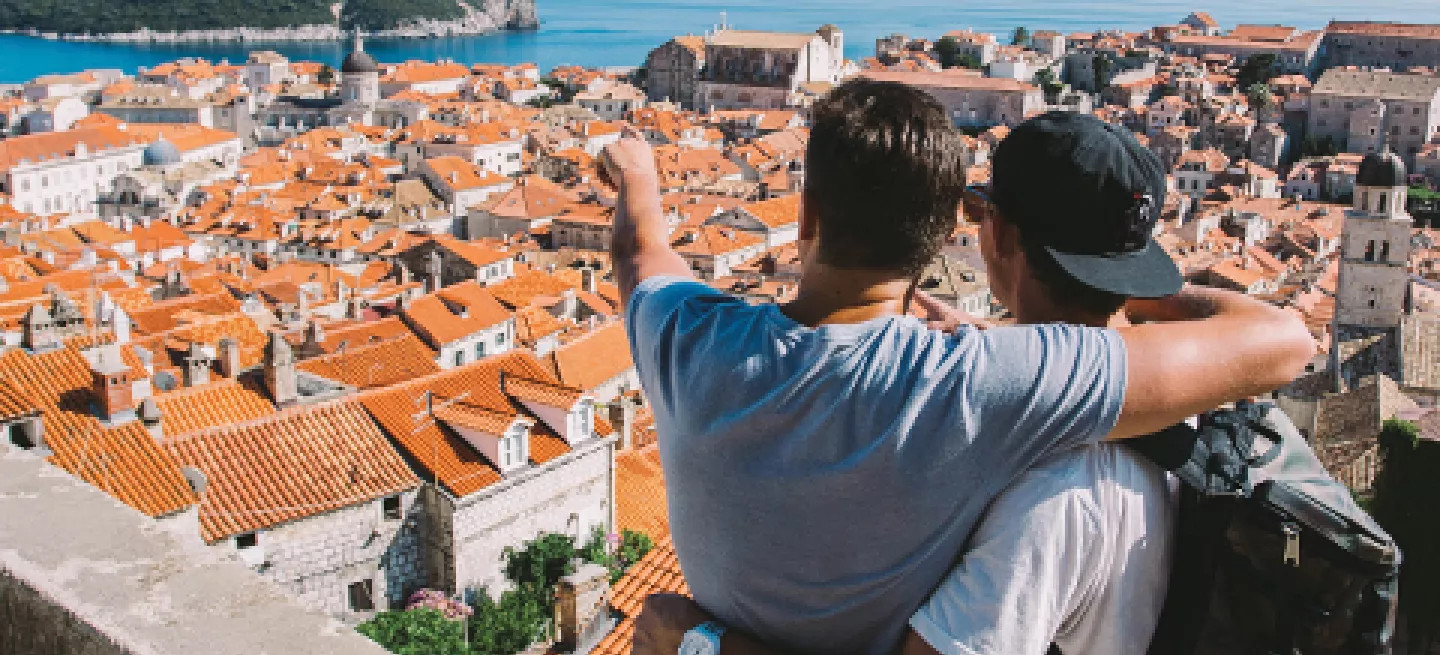 Two people with their arms around each other look out over orange rooves of Croatian town.