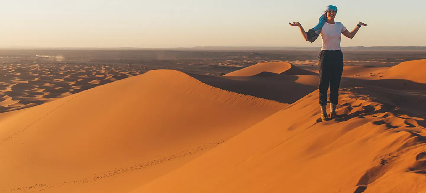 Person standing on the ridge of a sand dune with their hands out.