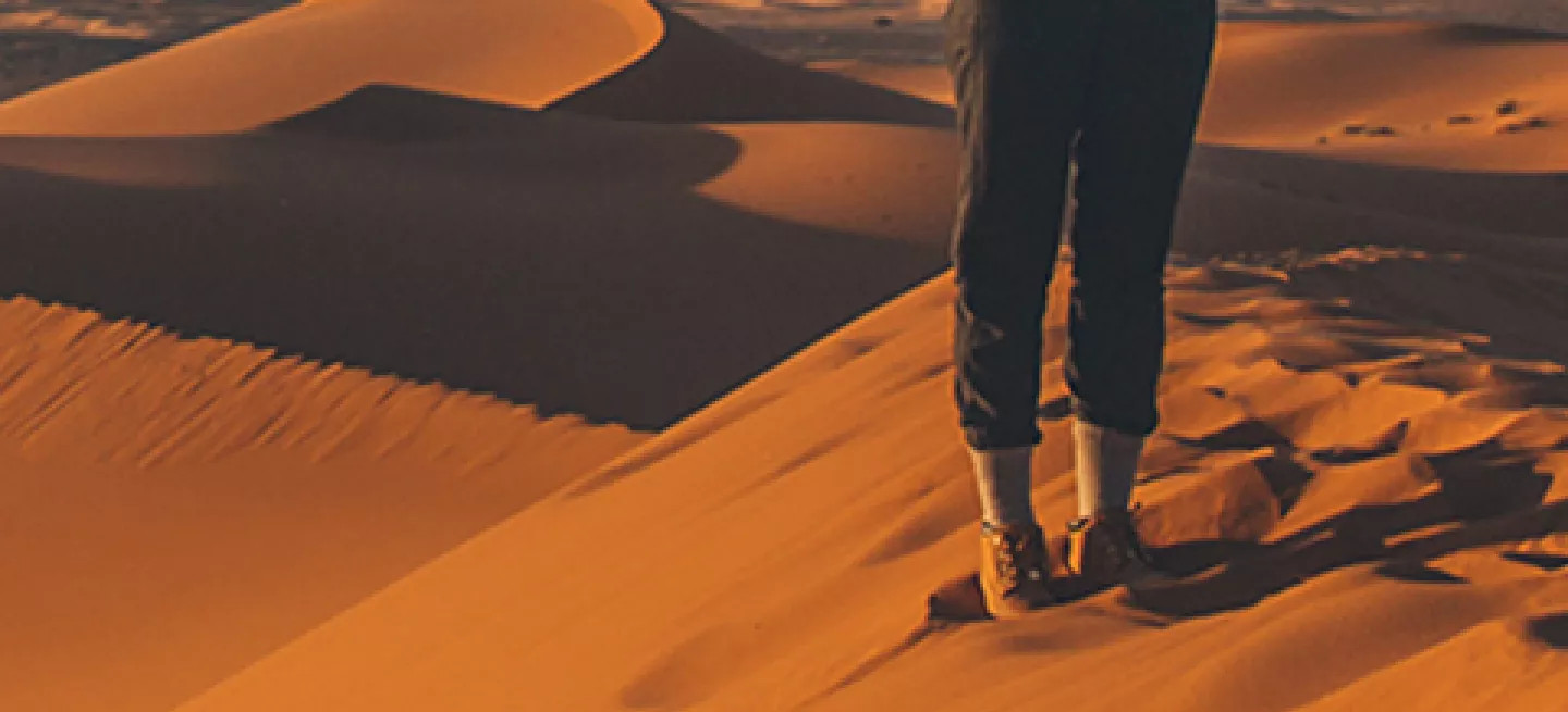 Person standing on the ridge of a sand dune with their hands out.
