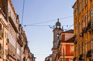 Colorful buildings surround enclose the street on a sunny afternoon in Lisbon.