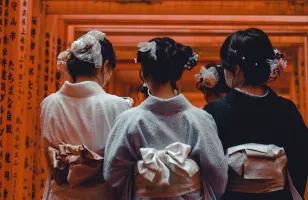 Three ladies in a kimono walking under Torii gates at the Fushimi Inari Shrine.