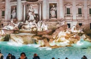 The famous Trevi Fountain of Rome lit up at night with a crowd of people surrounding it.