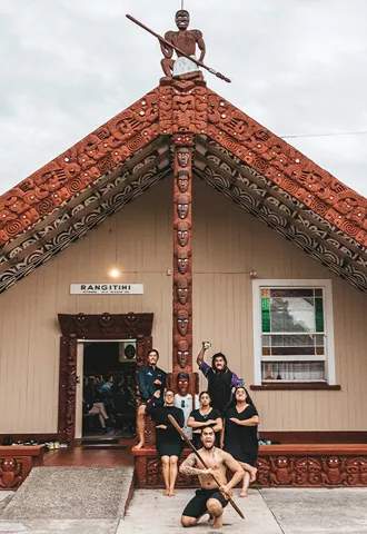 People holding a traditional pose in front of a Maori marae in New Zealand.