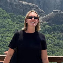 Person wearing sunglasses smiles with the view of a hill behind them.