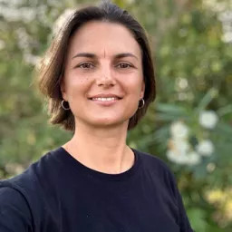 Person wearing black t-shirt smiles with the view of a hill behind them.