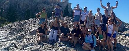 Topdeck tour group posing for a group photo on a hill in Athens with the Parthenon in the background.